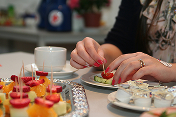 Foto: Ein Tisch mit Obstspießen und anderen Lebensmitteln sowie  ein Teller mit den Händen einer Frau, die isst.